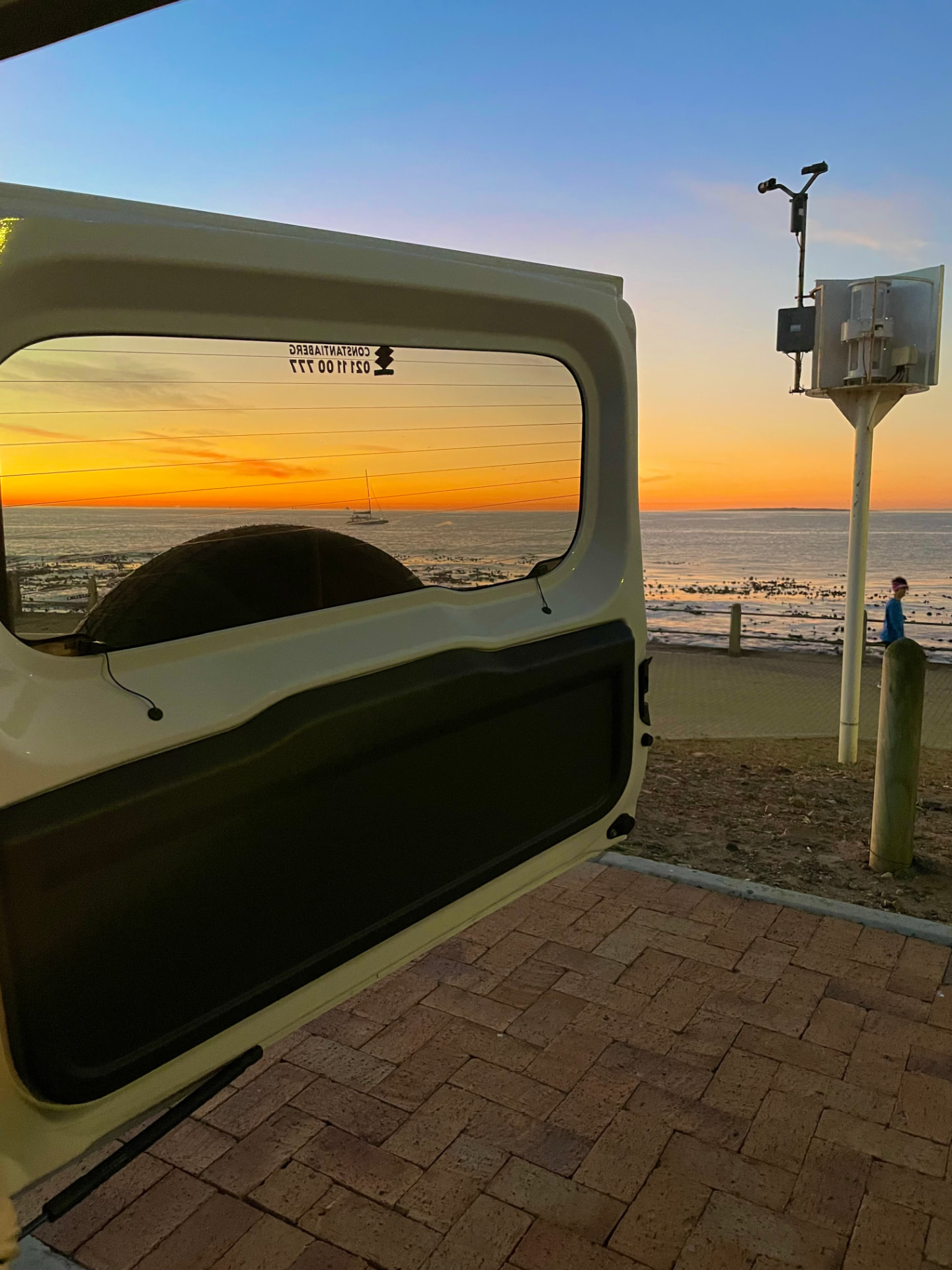 Sunset over the ocean framed through the open rear door of a parked car