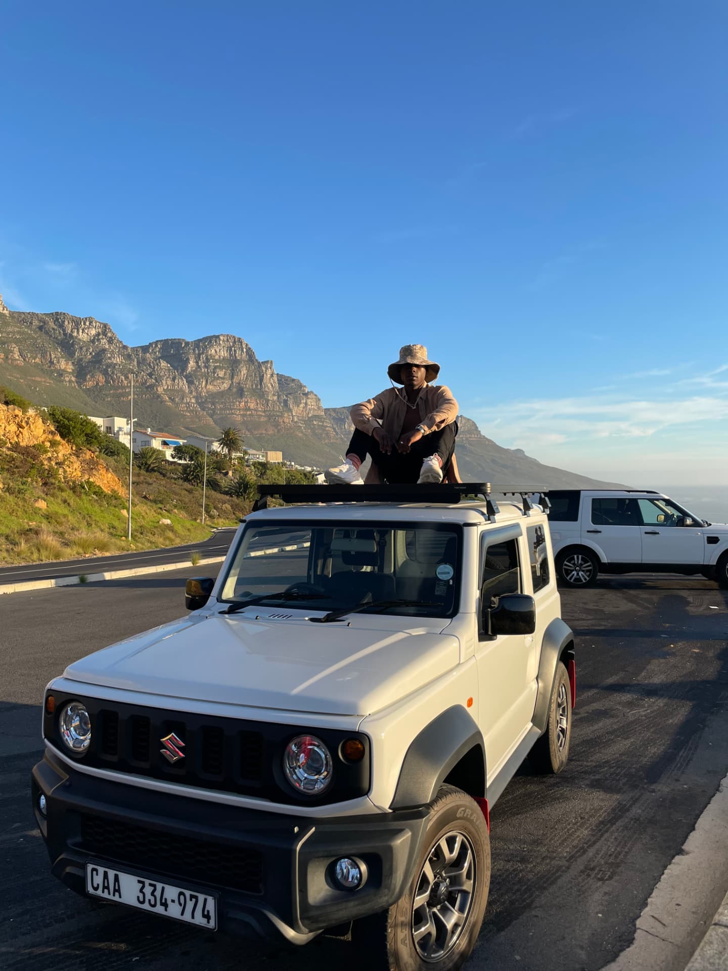 Sitting on the roof rack of a white 4x4 parked below a mountain ridge at golden hour